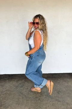 Side profile of the stretchy denim barrel overalls showing the relaxed fit and adjustable strap detail.