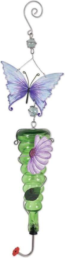 A hanging 28-inch green glass hummingbird feeder with a decorative metal purple butterfly and flower accent in a garden setting.