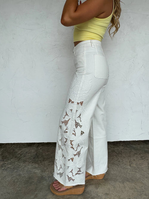Side view of Blakeley white wide-leg jeans showing the intricate laser-cut lace and embroidered floral side panel.