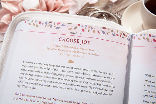 Open book with inspirational text on a table with flowers and a cup of coffee.
