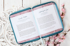 Open book with pink floral design on a decorative white surface with flowers.