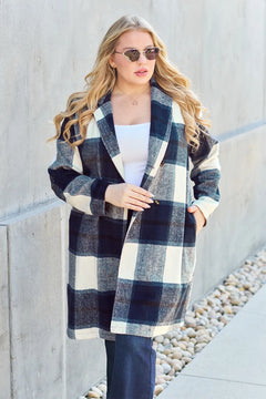 Woman wearing a plaid coat standing against a concrete wall.