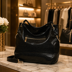 A black textured leather hobo handbag with gold-tone hardware, resting on a marble counter inside a boutique setting. Back-side