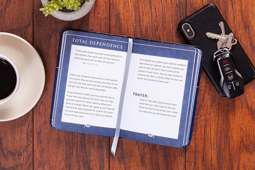 Open notebook with text on a wooden table with a coffee cup, phone, and keys.