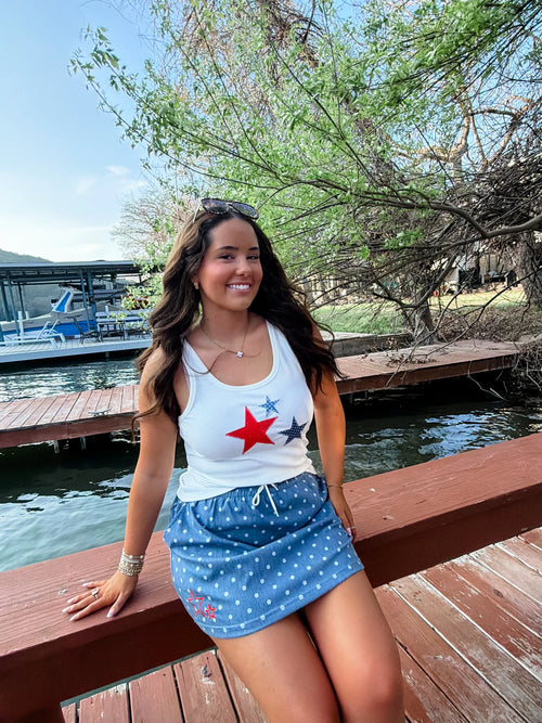 Woman wearing a white ribbed, stretchy tank top featuring printed star patches in red and blue.