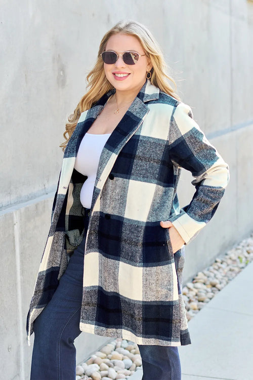 Woman wearing a plaid coat standing against a light-colored wall.