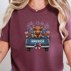 Heather maroon graphic tee featuring a highland cow in a vintage truck with America text, fireworks, florals, and American flags.
