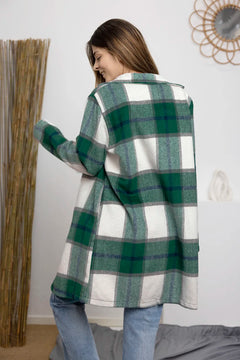 Woman wearing a green and white plaid coat in a room with a mirror and plant.