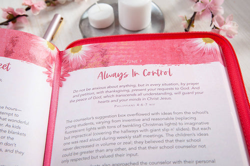Open book with pink floral design on a red cover, placed on a surface with candles and flowers.