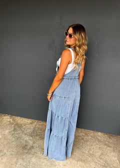 Woman wearing a long denim dress against a gray wall.