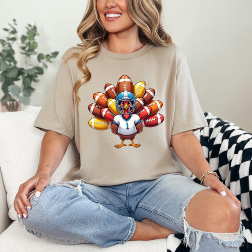 Woman wearing a beige t-shirt with a turkey football player graphic, sitting on a couch.