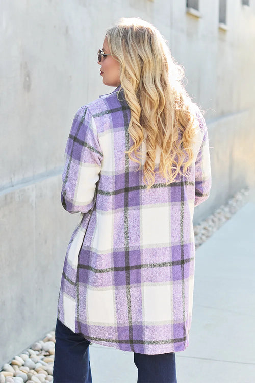 Person wearing a purple and white plaid coat standing against a light-colored wall.