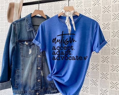 Blue t-shirt with 'autism accept. adapt. advocate.' text on a hanger with denim jacket and beige cap.