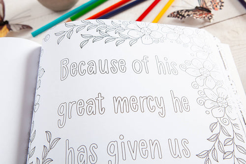 Coloring book page with text and floral designs on a table with coloring supplies.