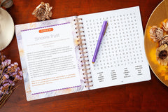 Open spiral-bound book with a word search puzzle on a wooden surface with decorative elements.