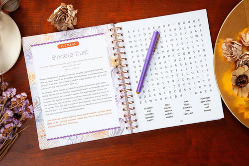 Open spiral-bound book with a word search puzzle on a wooden surface with decorative elements.