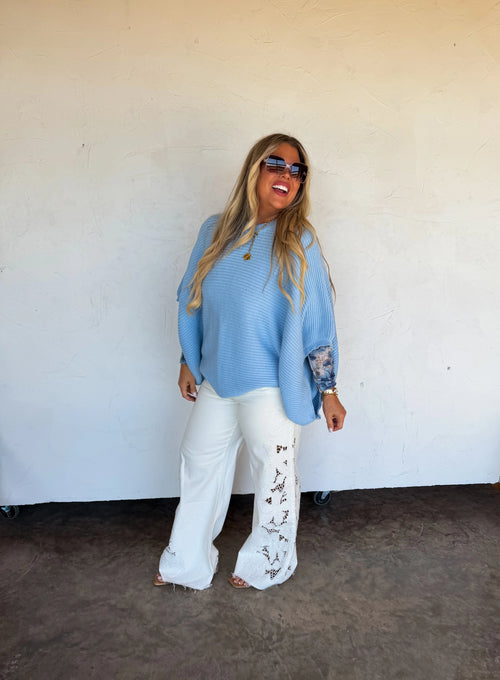 Model wearing white floral charm wide-leg jeans styled with a light blue poncho sweater.