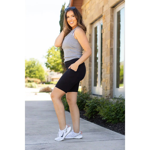 Side profile of woman modeling The Bree black biker shorts with her hand in the functional side pocket, showing phone-ready storage.