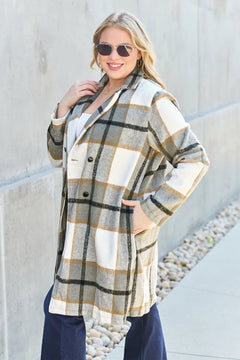 Woman wearing a plaid coat standing against a light-colored wall.