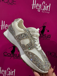 White sneaker with rhinestone embellishments held against a pink background with 'Hey Girl by Corkys' branding.