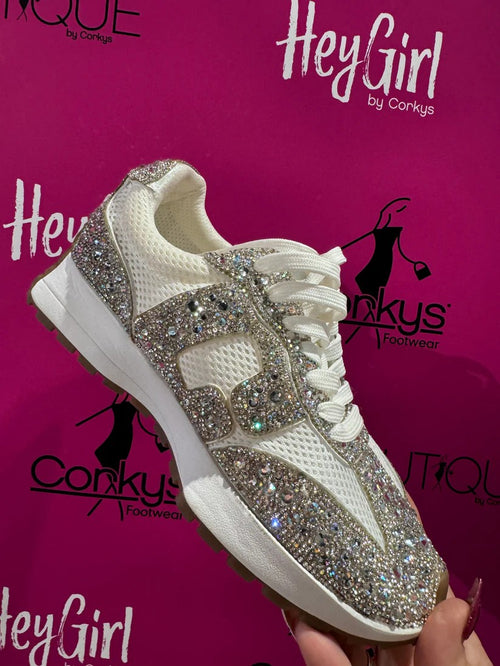 White sneaker with rhinestone embellishments held against a pink background with 'Hey Girl by Corkys' branding.