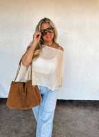 Woman wearing sunglasses and holding a brown handbag against a white wall.