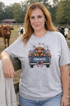 Ash gray graphic tee featuring a highland cow in a vintage truck with America text, fireworks, florals, and American flags.