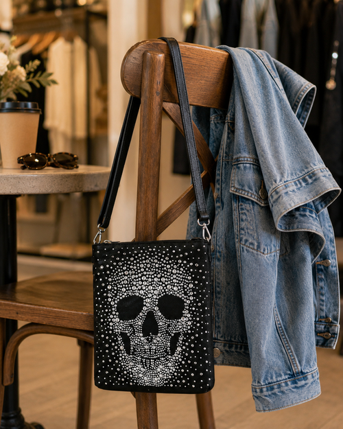 Black handbag with skull design on a wooden chair in a store setting