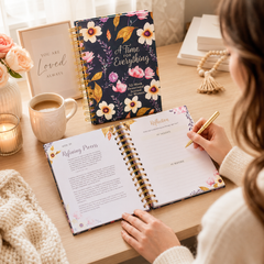 Person using a floral planner with a cup of coffee and candles on a table.