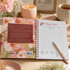 Open spiral-bound notebook with floral design on a wooden surface with a candle and cup in the background.