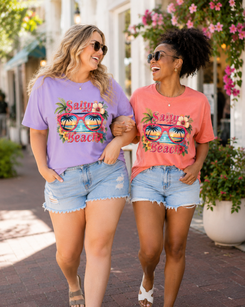 Two women walking together, each wearing a 'Salty Beach' t-shirt with sunglasses graphics.