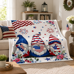 Patriotic gnome blanket draped over a beige couch in a cozy living room with Americana decor and red white and blue accents.