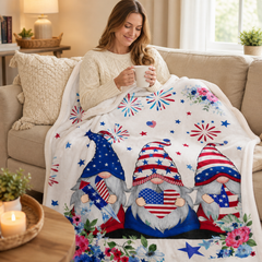Woman relaxing on a couch with a patriotic gnome blanket while holding a mug in a cozy living room setting.