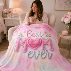 Woman relaxing in a cozy chair with a mug and a pink Best Mom Ever fleece throw blanket draped over her lap in a soft bedroom setting.