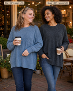 Two women standing outdoors at a cafe wearing oversized crewneck sweaters, one in dusty blue and one in charcoal gray. Text labels at the top indicate names and sizes: 'Rita | 5'6" | wears L/XL' and 'Maya | 5'6" | wears S/M'.