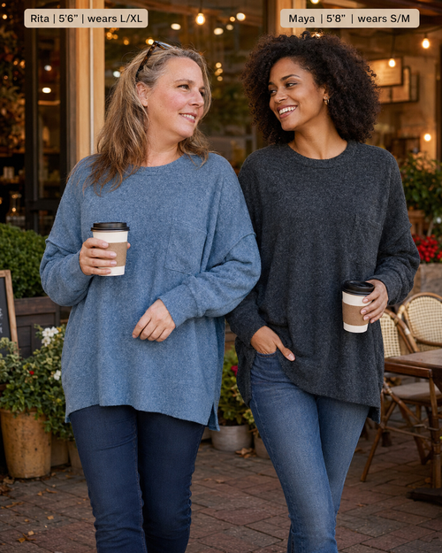 Two women standing outdoors at a cafe wearing oversized crewneck sweaters, one in dusty blue and one in charcoal gray. Text labels at the top indicate names and sizes: 'Rita | 5'6" | wears L/XL' and 'Maya | 5'6" | wears S/M'.
