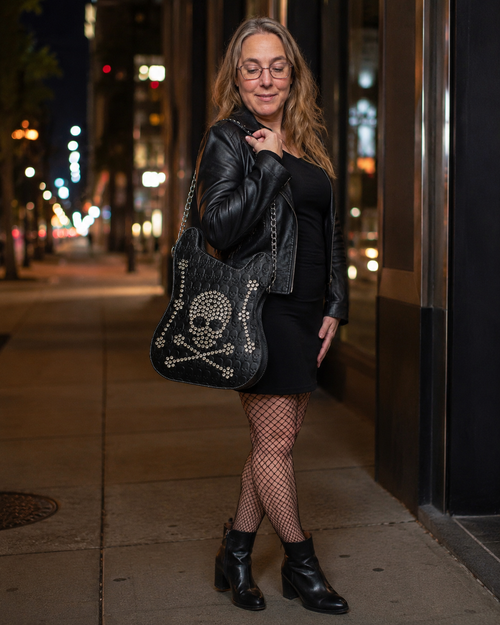 Woman in black outfit with skull-patterned bag on a city street at night