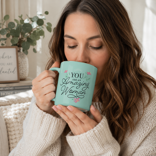 Woman in a cozy cream sweater drinking from a teal You Are An Amazing Woman ceramic mug.