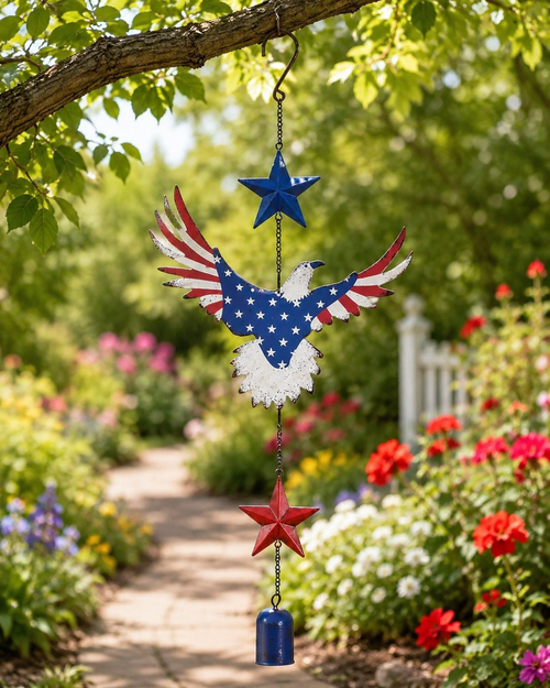 Americana eagle garden hanging chime hanging from a tree branch above a colorful flower garden path.