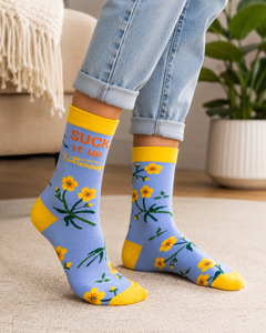 Close-up of woman wearing cuffed jeans and light blue Suck It Up Buttercup crew socks with yellow cuffs, toes, and floral design.