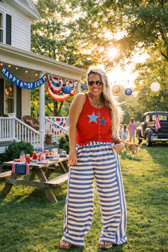 Woman in red top and striped pants standing in a backyard with July 4th decorations.
