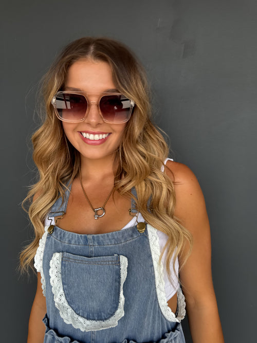 Woman wearing sunglasses and a denim dress with lace details against a gray background