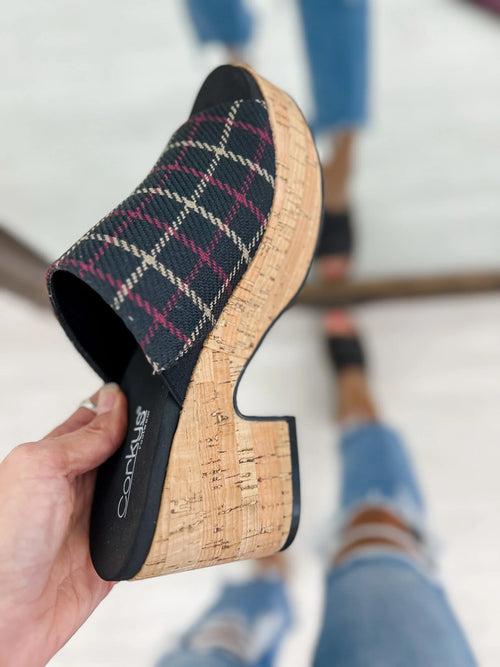 Plaid wedge sandal held by a hand with blurred background