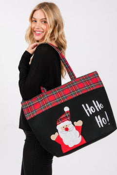 Person holding a black tote bag with red plaid accents and a Santa Claus graphic, on a white background.