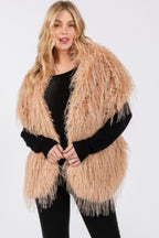 Model wearing the Glam Getaway Faux Fur Pull-Through Shawl in tan faux fur, styled over a black outfit.