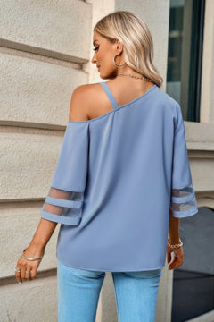 Woman wearing a light blue off-shoulder top with sheer sleeves against a building background