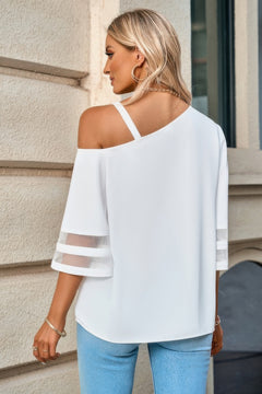 Woman wearing a white off-shoulder top with sheer sleeves against a building background