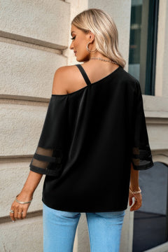 Woman wearing a black off-shoulder top with sheer sleeves against a building background
