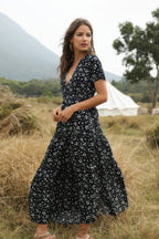 Woman in a black floral dress standing in a field with mountains in the background