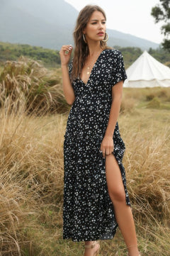 Woman in a black floral dress standing in a grassy field with a tent in the background